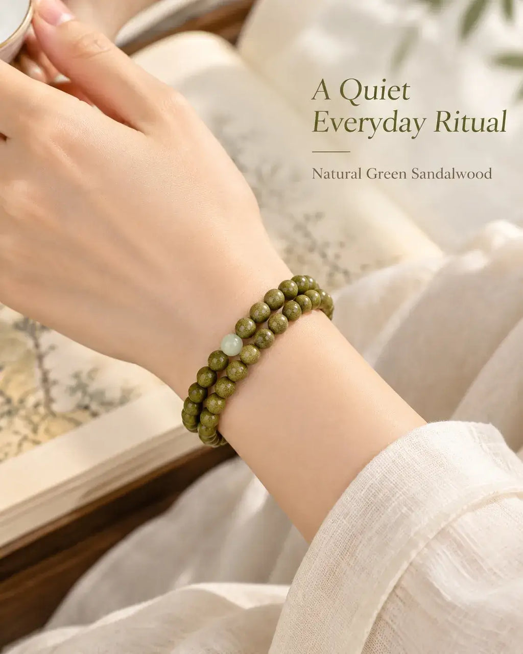Two rows of green sandalwood beads worn on the wrist beside a cream sleeve