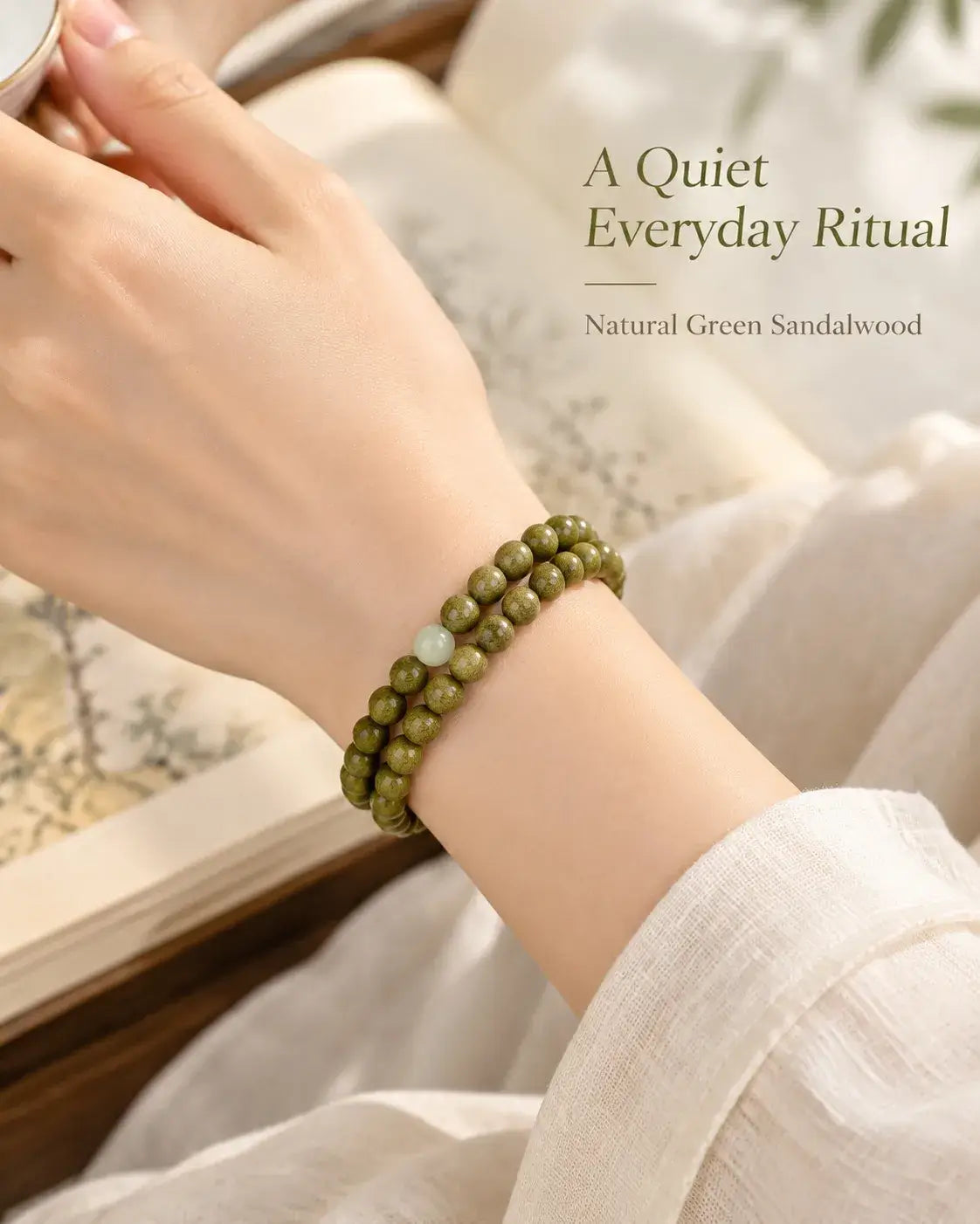 Two rows of green sandalwood beads worn on the wrist beside a cream sleeve